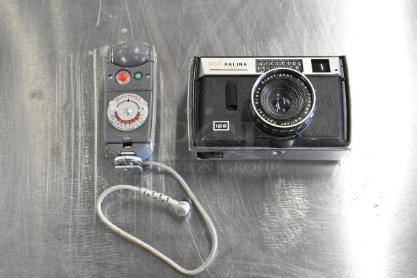Halina 1:5.6 film camera and Honeywell Tilt-a-mite gauge on a metal surface, showing lens and dials, vintage condition.