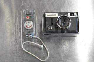 Halina 1:5.6 film camera and Honeywell Tilt-a-mite gauge on a metal surface, showing lens and dials, vintage condition.