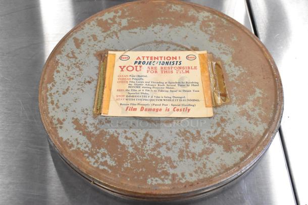 Vintage metal film reel case with label stating projectionists' responsibilities for film care. Rusted exterior.