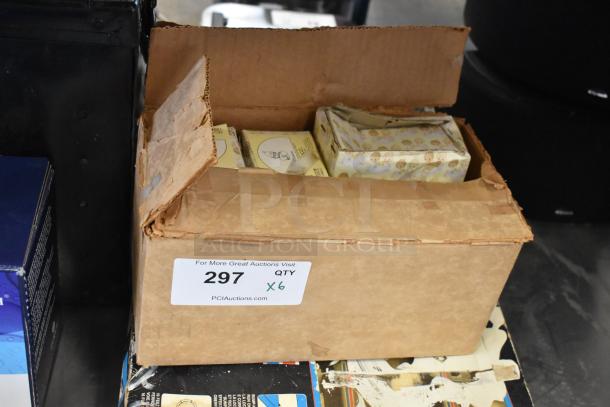 Cardboard box containing six Precious Moments figurines in original packaging, includes clowns and "Winter's Song," with auction label.