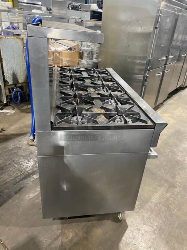U.S. Range commercial stainless steel 10-burner range with double oven, equipped with a backsplash, overhead salamander shelf, and casters.