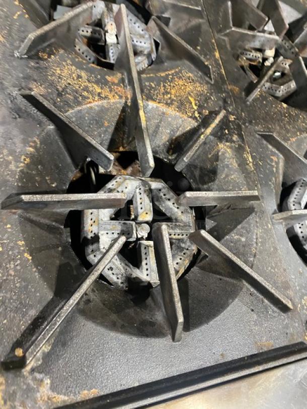 U.S. Range commercial gas 10-burner stove top, stainless steel, showing wear. Includes grates.