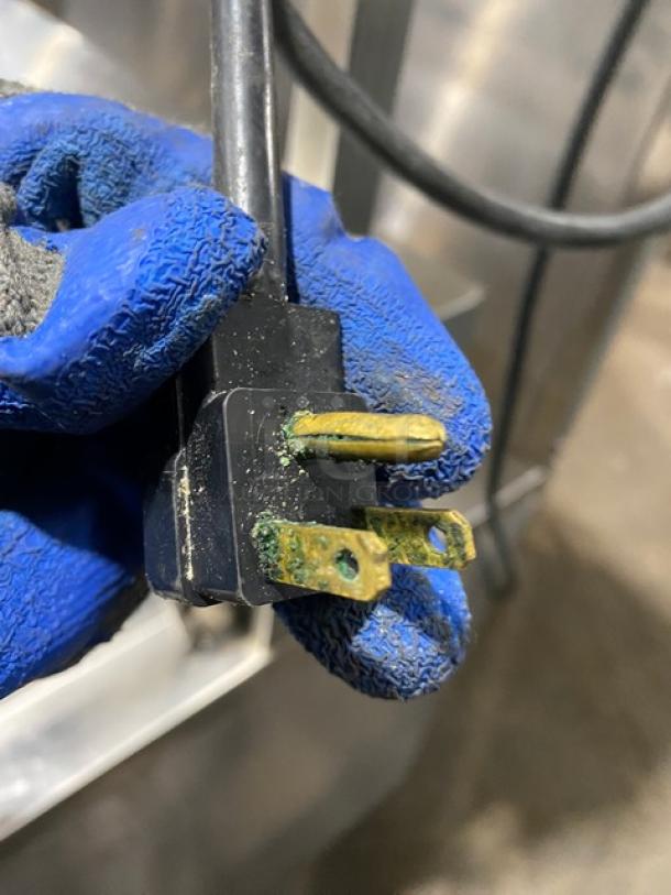 Close-up of a power plug with corrosion on the prongs, held by a gloved hand. Ensure safe use before connecting.