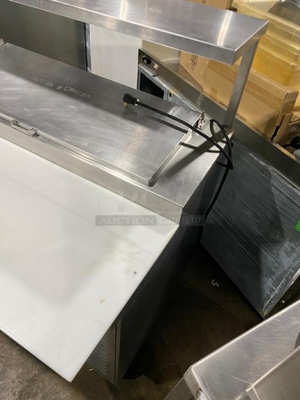 Traulsen TRP096S stainless steel 3-door pizza prep table with cutting board, overhead shelf, and poly-coated racks, on casters.