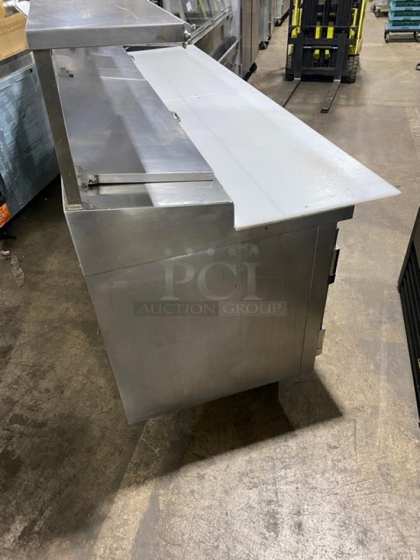 Traulsen TRP096S stainless steel 3-door refrigerated pizza prep table with cutting board, overhead shelf, and wired racks, on casters.