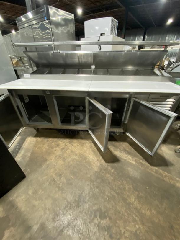 Traulsen TRP096S stainless steel 3-door pizza prep table with cutting board, overhead shelf, and poly-coated racks, on casters.