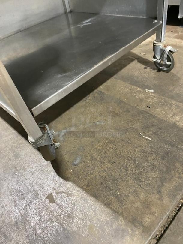Commercial stainless steel rolling kitchen utility table on casters, showing sturdy construction and wear on wheels.