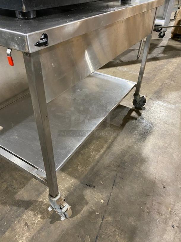 Commercial stainless steel table with lower shelf and caster wheels, durable and in good condition, suitable for kitchen use.