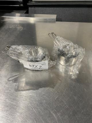 Set of new commercial stainless steel measuring cups, wrapped in plastic. Label shows "87 Qty 2."