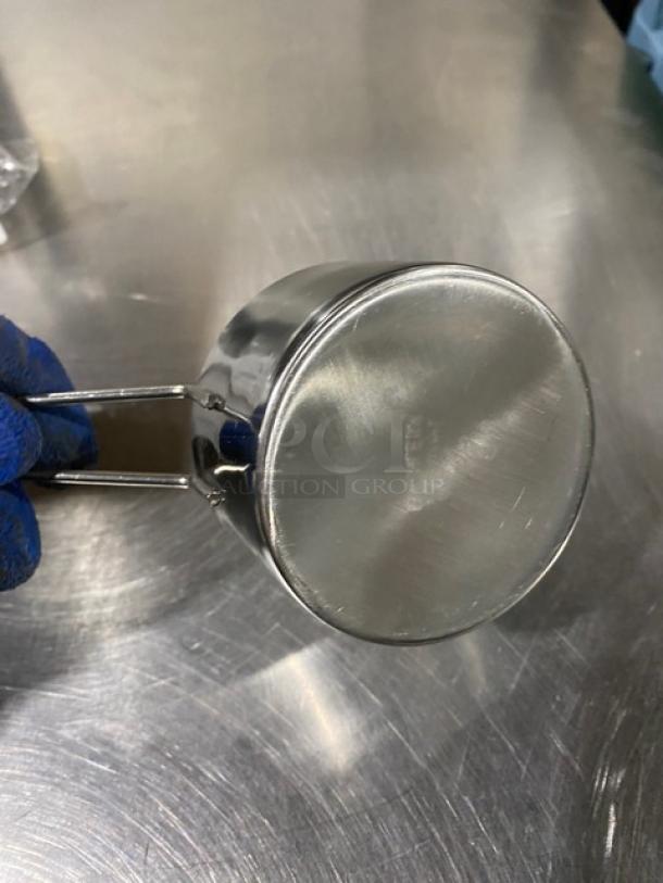 New stainless steel measuring cup, commercial grade, reflective finish, ergonomic handle, perfect condition.