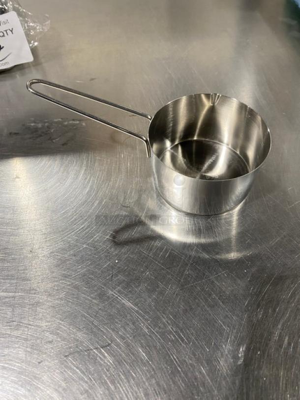 New commercial stainless steel measuring cup with handle on metal surface, reflecting light.
