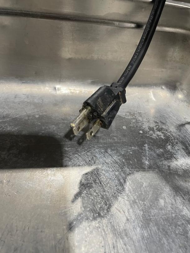 Serv-Ware EST3-1 hot food table plug, showing stainless steel texture and wear. Model SN: M1100228, 120V electric powered.