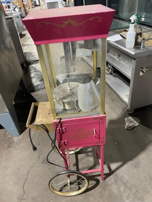 Great Northern Popcorn pink electric popcorn machine on casters and legs. Features ornate design and storage compartment.