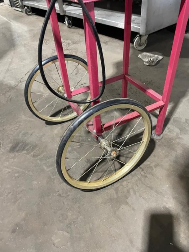 Great Northern Popcorn machine base in pink, on casters and legs, showing large metal wheels and sturdy frame.