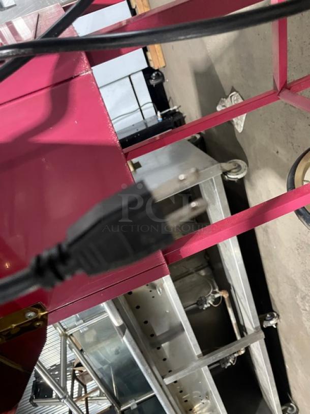 Great Northern Popcorn pink electric popcorn machine on casters and legs. Features durable construction, plug visible.