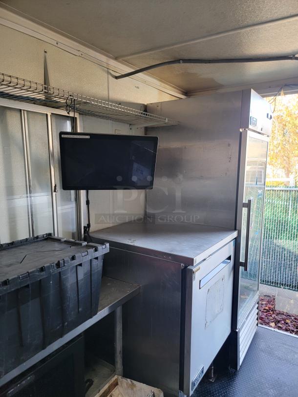 2020 16' Diamond Cargo food trailer interior with True refrigerator, prep table, and flat screen monitor. Clean, ready for use.