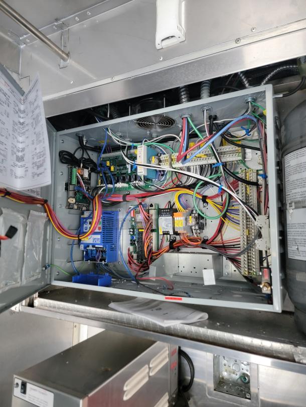 Interior wiring setup of a 2021 28' Texino Food Trailer. Visible are organized cables, circuit boards, and electrical components, indicating a well-maintained electrical system essential for mobile kitchen operation.