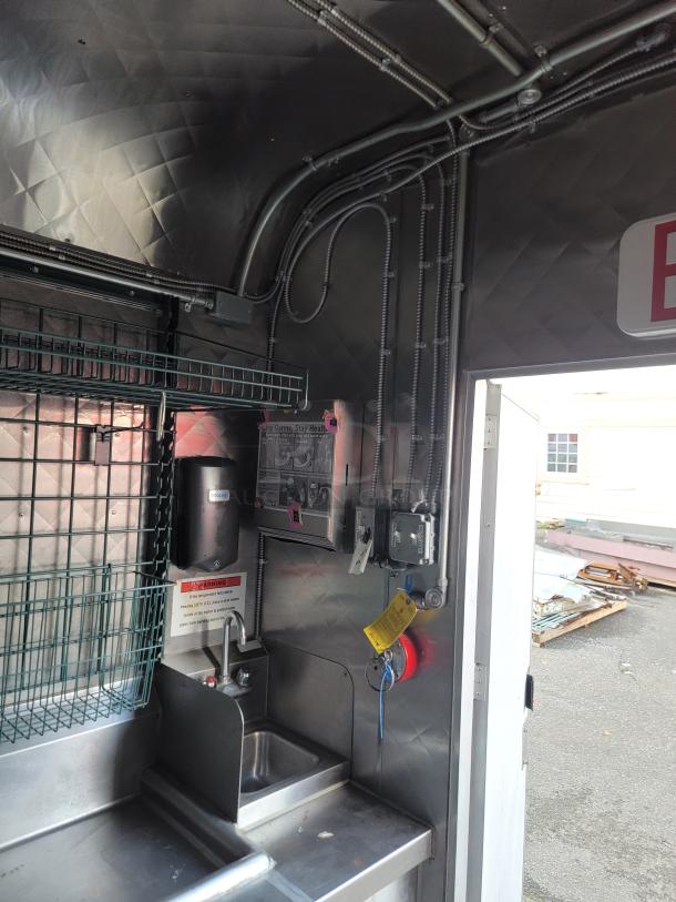 Interior of a 24' Quality food trailer with stainless steel walls, sink, and NSF-certified equipment. Wiring and signs visible.