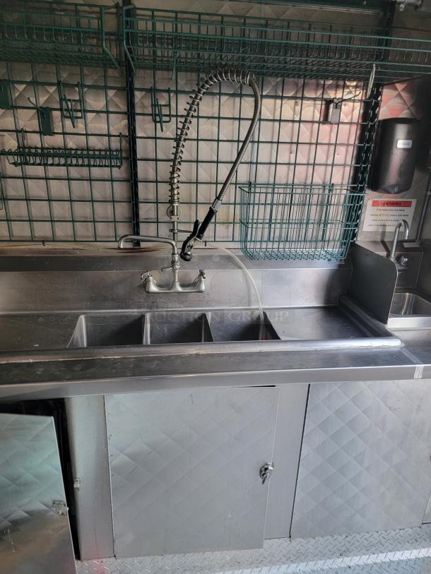 Quality 24' food trailer interior showing stainless steel sink, spray faucet, and shelving for culinary equipment.