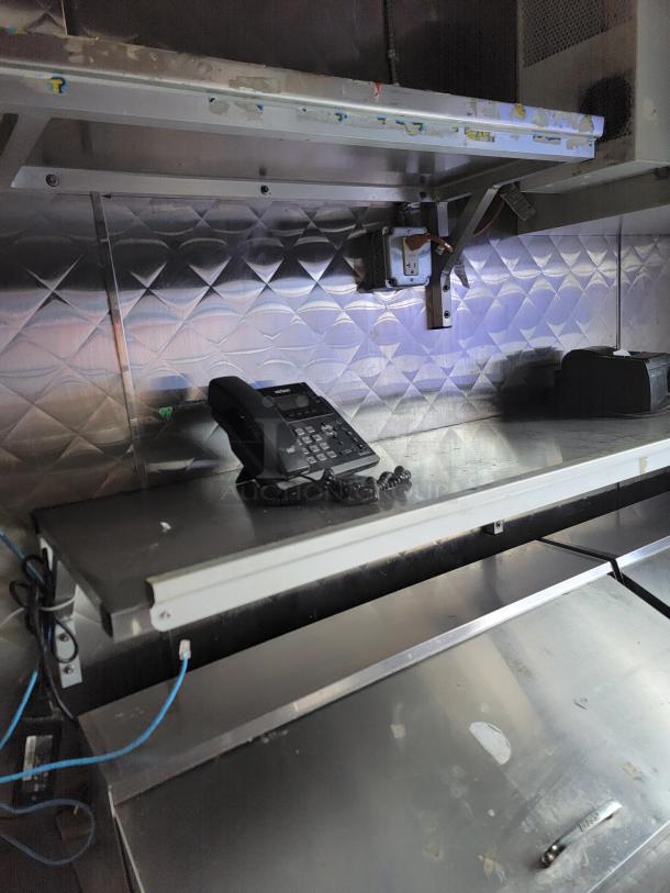 Interior of a 24' Quality food trailer showing stainless steel counters, shelves, and a phone. Ideal for high-volume service.