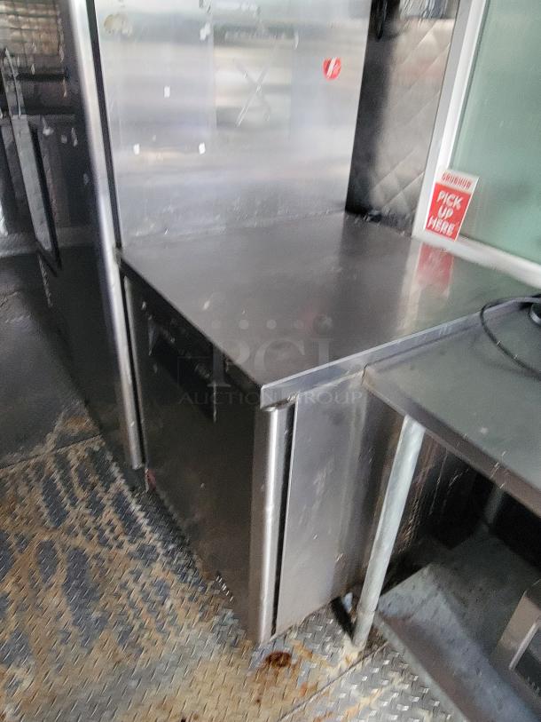 24' Quality Food Trailer interior with stainless steel surfaces, refrigeration unit, and pickup sign. Built 2020, fully-equipped.