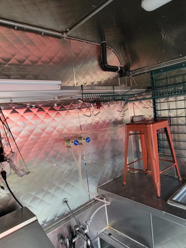 Interior of 2020 Quality 24' food trailer, featuring stainless steel walls, sink area, and utility hooks. Clean and well-maintained.