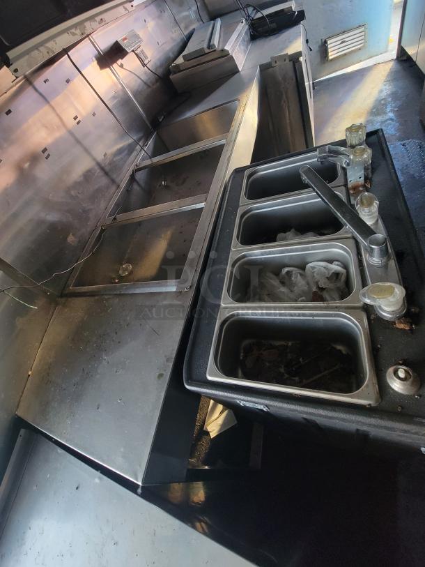 2019 Quality 24' food trailer interior, featuring metal prep counters and a multi-compartment sink. Well-equipped kitchen area.