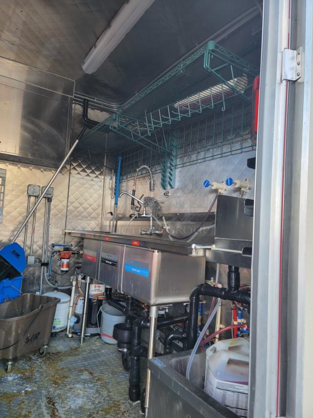 2021 28' Rock Solid Cargo mobile kitchen trailer interior with three-compartment sink, commercial plumbing, and storage shelves.