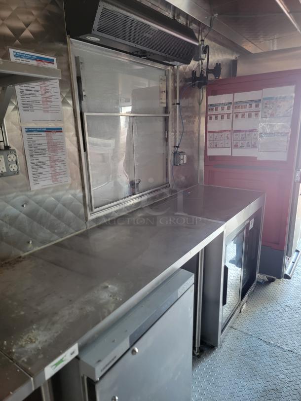 Interior of 2021 28' Rock Solid Cargo Mobile Kitchen Trailer. Features stainless steel counters, refrigeration units, ventilation system, and instructional posters.