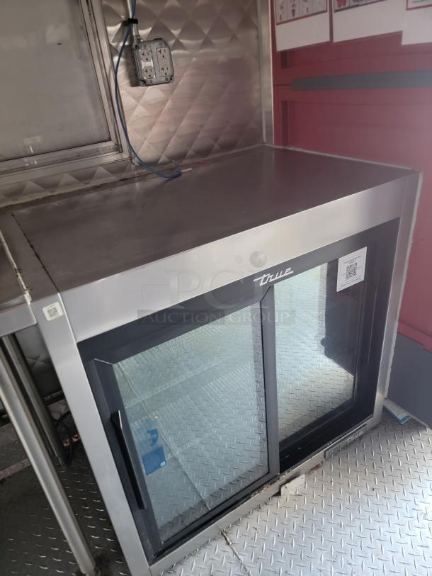 Rock Solid Cargo 28' Mobile Kitchen Trailer interior, showcasing a True commercial refrigerator under a stainless steel counter.