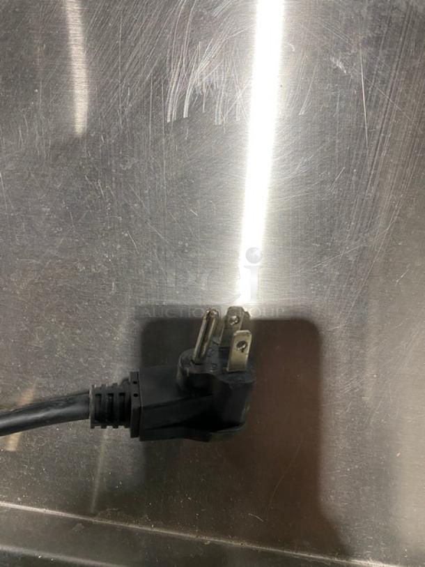 Power cord for Silver King SKEPT4812SD1BM commercial prep table, black, three-prong plug, against stainless steel surface.
