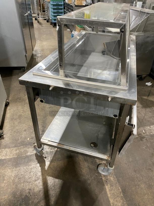 Delfield N8156B stainless steel refrigerated salad bar with sneeze guard, folding tray slide, and undershelf on casters.