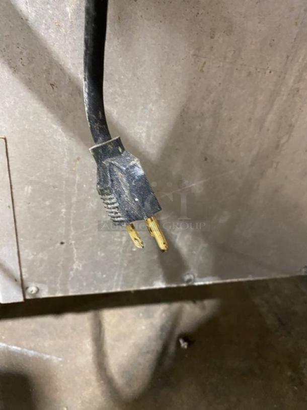 Close-up of a power plug attached to a large, stainless steel commercial appliance. The plug is worn and the metal prongs are visible.