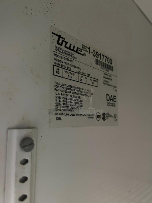 Label on True GDM-45-HC-LD merchandiser shows model details, voltage (115v), and refrigerant information. Marks some wear.
