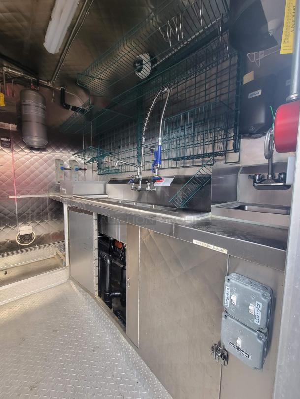 2021 16' mobile ghost kitchen interior, featuring stainless steel surfaces, three-compartment sink, and vent fan switch.