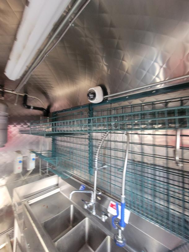 Interior of 2021 Quality 16' mobile commercial kitchen trailer, featuring stainless steel sink with pre-rinse sprayer and shelving.