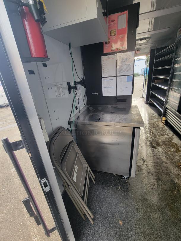 Interior of 2021 SDG food trailer with stainless steel counter, electrical outlets, red fire extinguisher, and folding chairs.