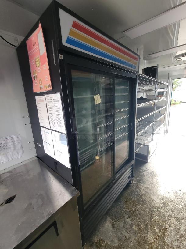 Inside view of 2021 SDG 'Goodees' trailer showing a large True Refrigeration display case, stainless steel countertop, and chrome wire shelving.