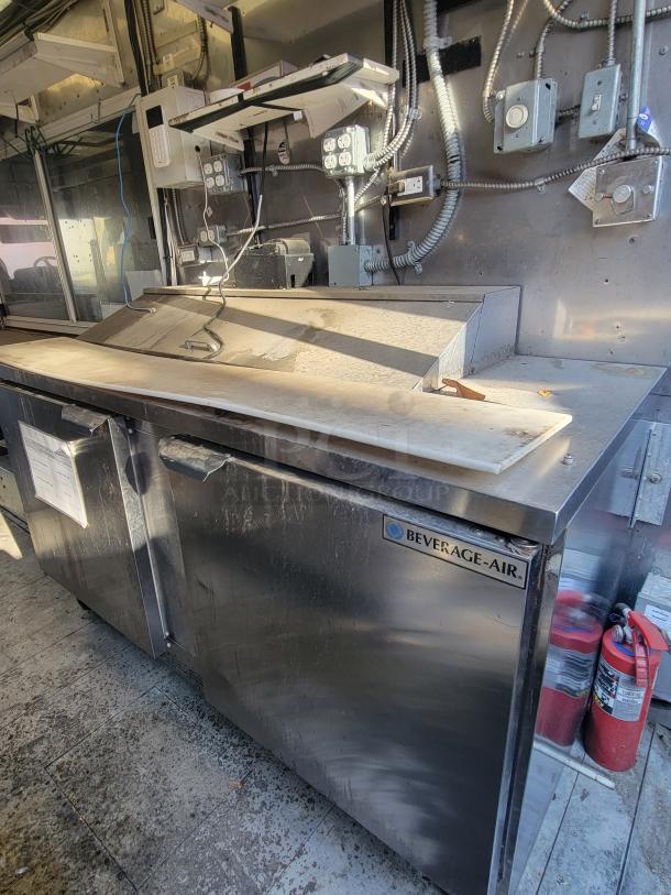 Freightliner MT45 mobile kitchen interior with stainless steel Beverage-Air prep table, wiring, and fire extinguishers visible.