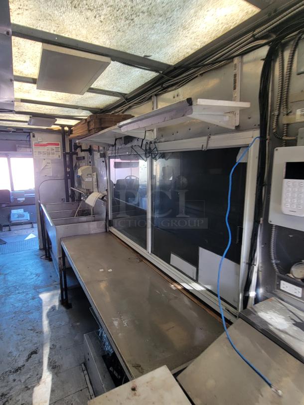 Interior of a 2004 Freightliner MT45 mobile kitchen showing stainless steel countertops, large sinks, and electrical setup.