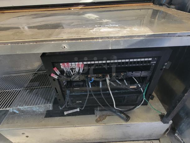 Network rack inside 2004 Freightliner MT45 Mobile Kitchen with APC UPS and cables. Stainless steel surfaces above.