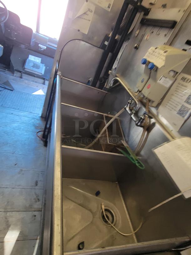 Stainless steel three-compartment sink inside a 2004 Freightliner MT45 mobile kitchen, featuring plumbing setup and control panel.