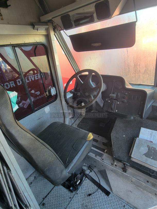 Interior of a 2004 Freightliner MT45 Step-Van driver's cabin, showing a worn driver's seat, steering wheel, and control panel with visible wear.
