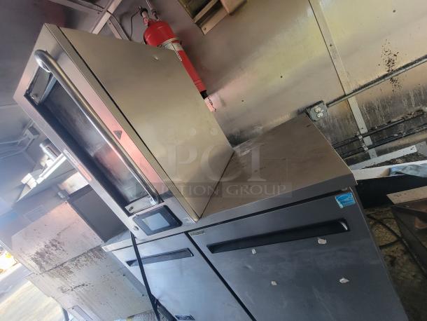Interior view of a 2020 24' Diamond Cargo mobile ghost kitchen trailer. Features stainless steel equipment, built-in fire suppression, and commercial-grade cooking appliances. Visible is a commercial oven with a fire extinguisher above it.
