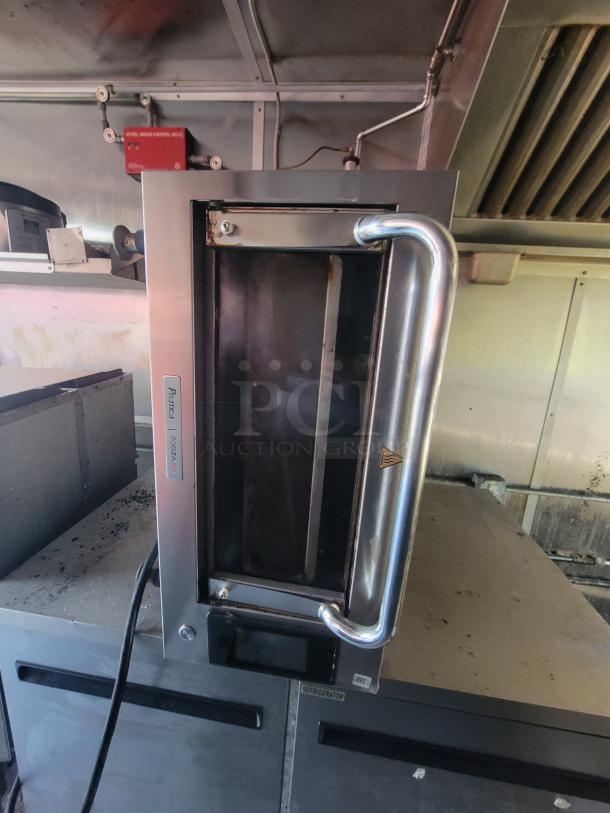 Commercial-grade stainless steel cooking appliance inside a mobile kitchen trailer. Features include reinforced handle and control panel.