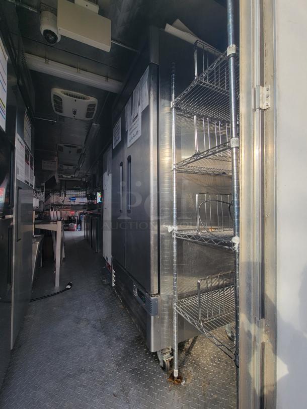 2022 Titanium Cargo 28' Food Trailer interior with commercial kitchen equipment, including refrigerators, griddle, and storage racks.