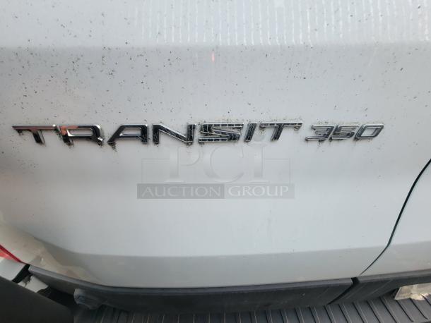 2021 Ford Transit 350 Cargo Van badge on rear door, showing "Transit 350" text. Slight grime visible on white surface.