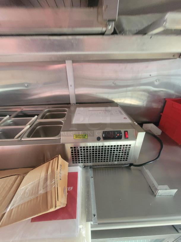 2022 Rock Solid 28' food trailer interior with new commercial-grade equipment, pristine stainless steel surfaces, natural refrigerant label.
