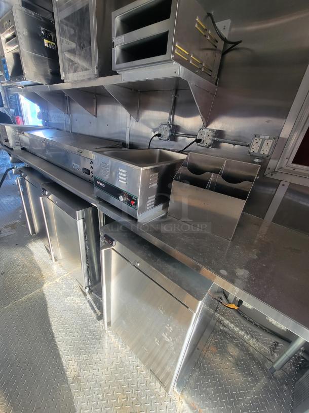 2021 Titanium 28' food trailer interior with new, unused equipment. Stainless steel shelves, appliances with protective material.