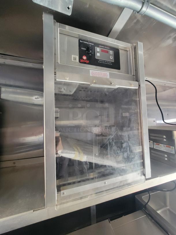 Professional-grade food trailer interior with stainless steel shelving and a wrap-protected new appliance, featuring control panel and Wendy's branding.